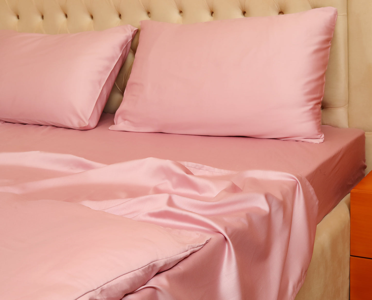 Pink quilt cover set with matching pillowcases on a beige upholstered bed